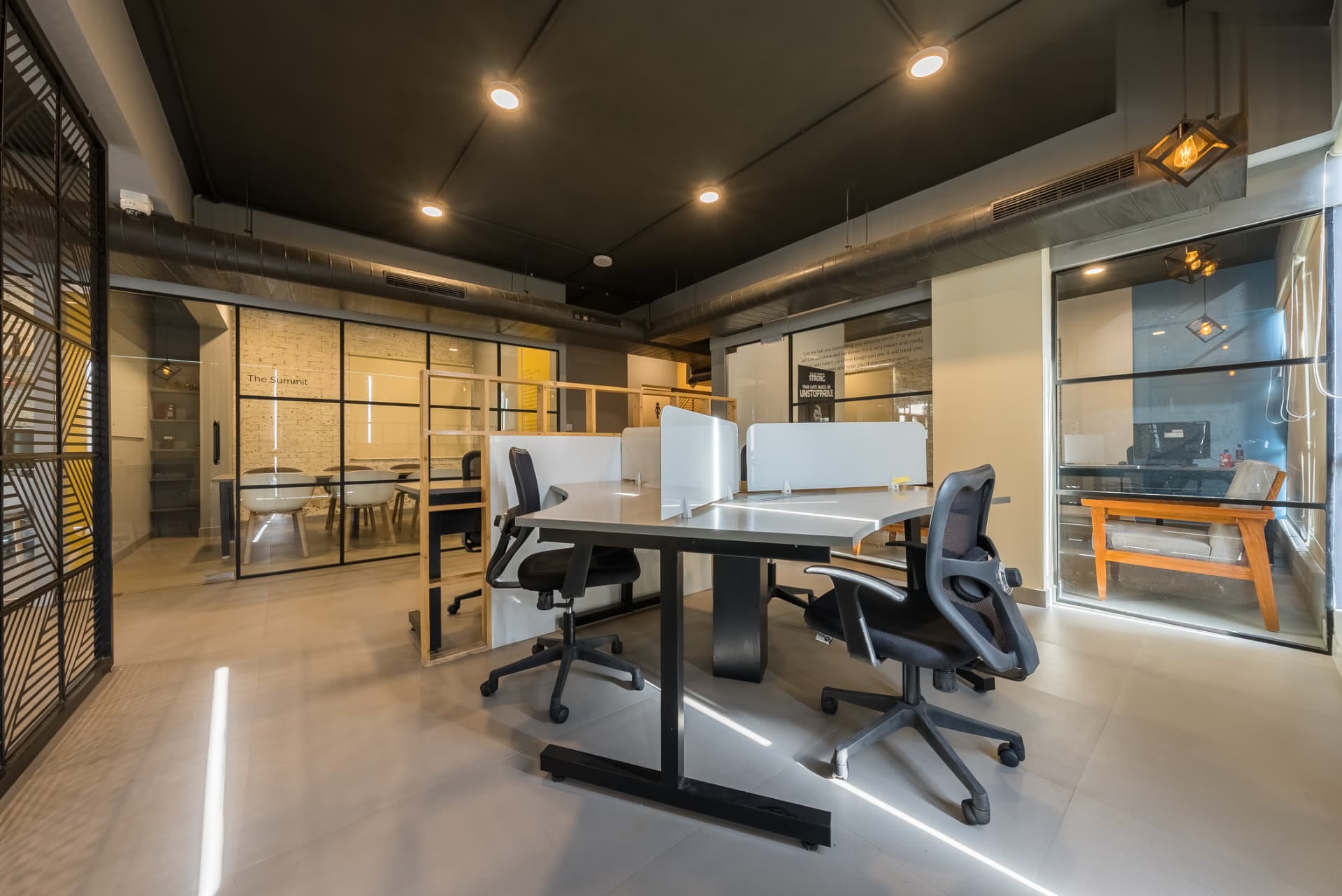 Open workspace with shared desks, acoustic screens and glass-walled cabins beyond