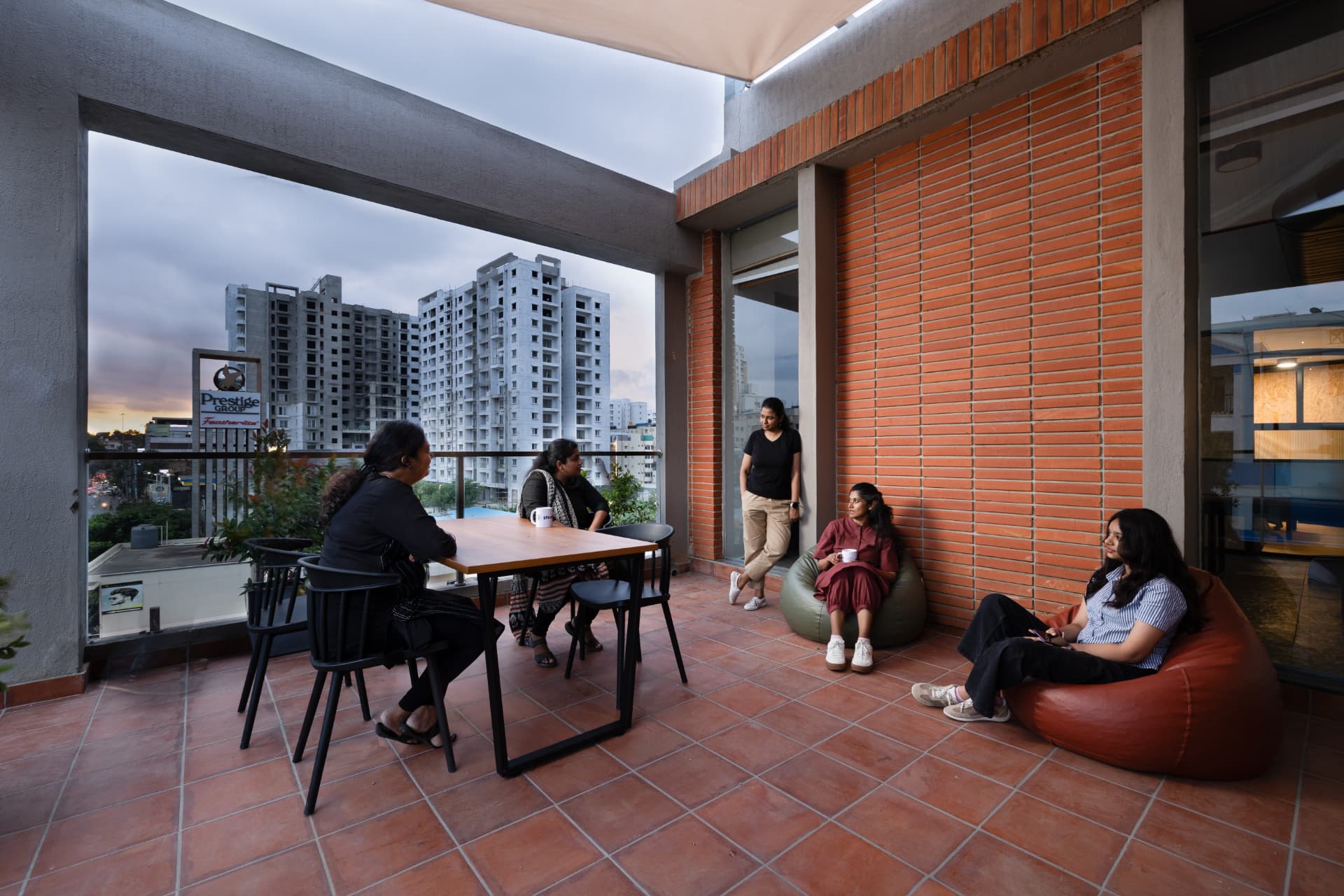 Planted balcony terrace at Steadwork ORR | Panathur with a dining table, bean bags and a city view at dusk