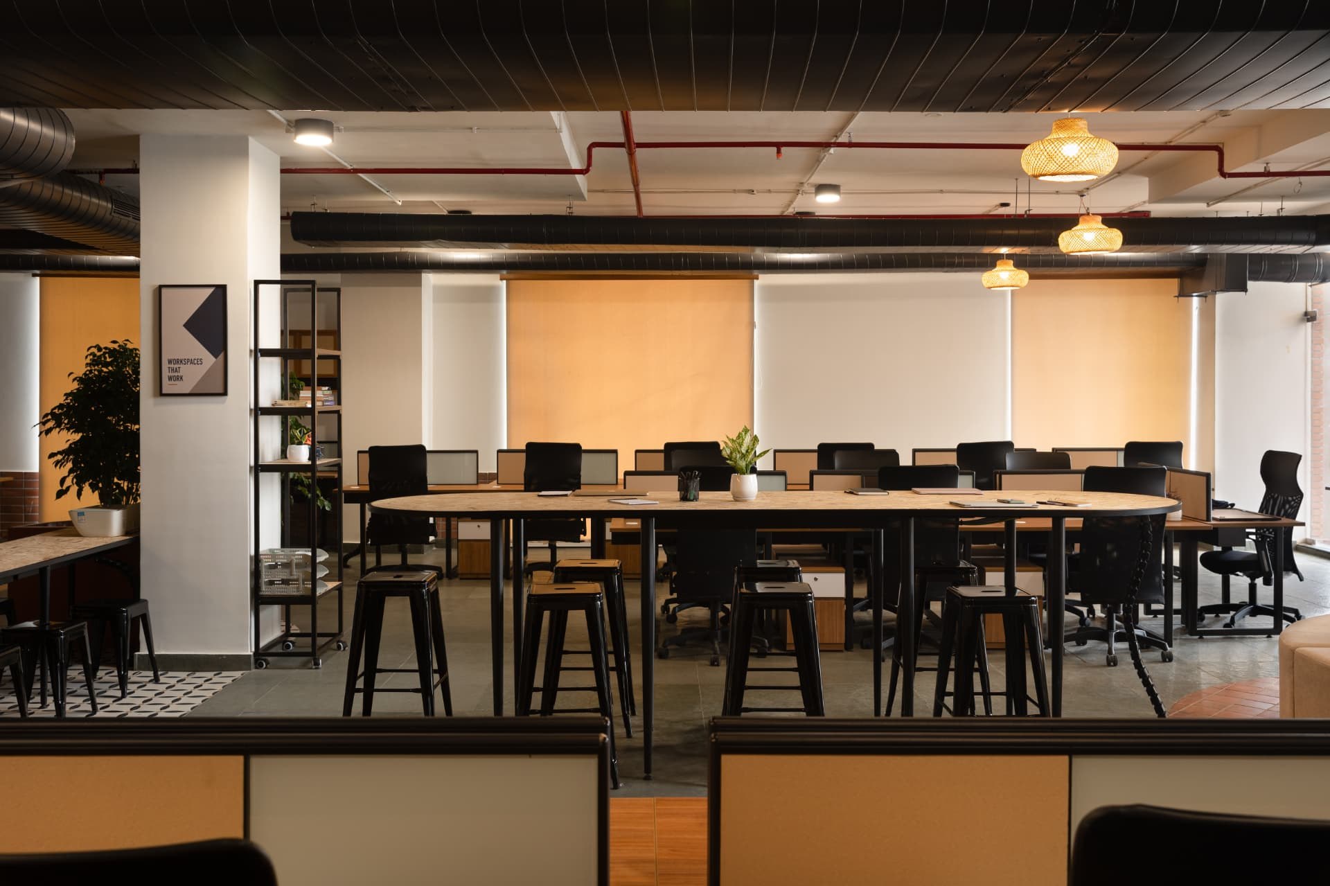 Workstation bays and a shared oval table under woven pendant lights at Steadwork