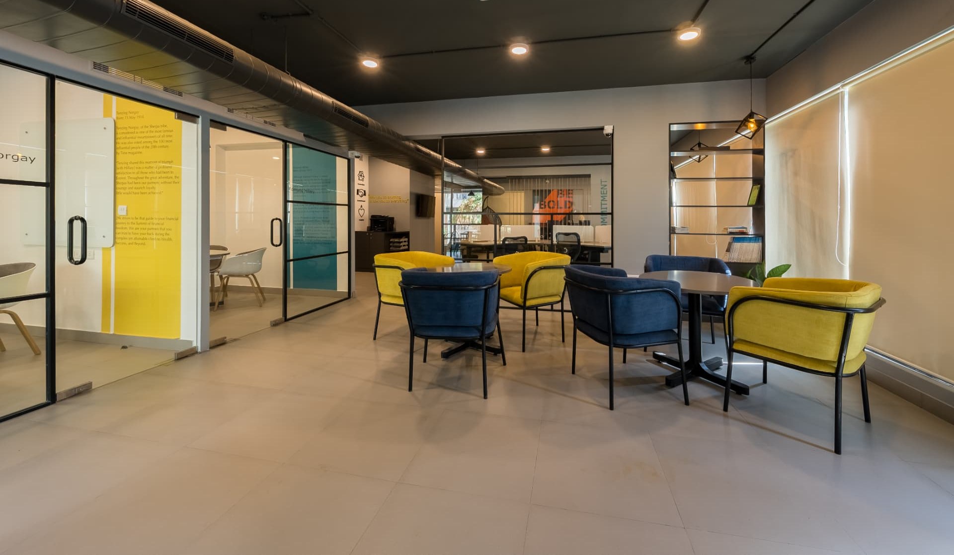 Breakout lounge on the first floor with yellow and blue armchairs beside glass-walled meeting rooms