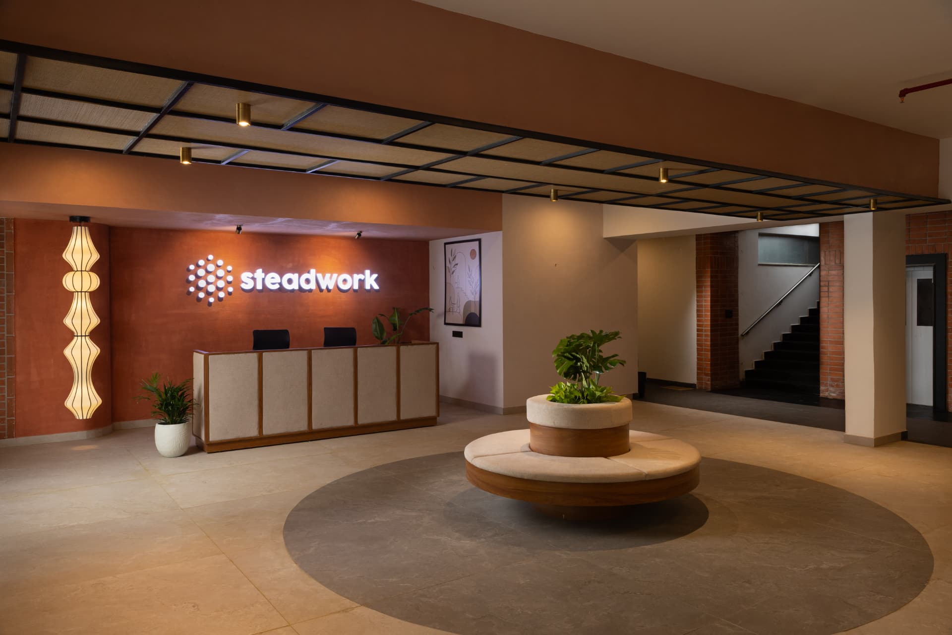 Reception lobby at Steadwork ORR | Panathur with an illuminated Steadwork sign and a circular planter seat